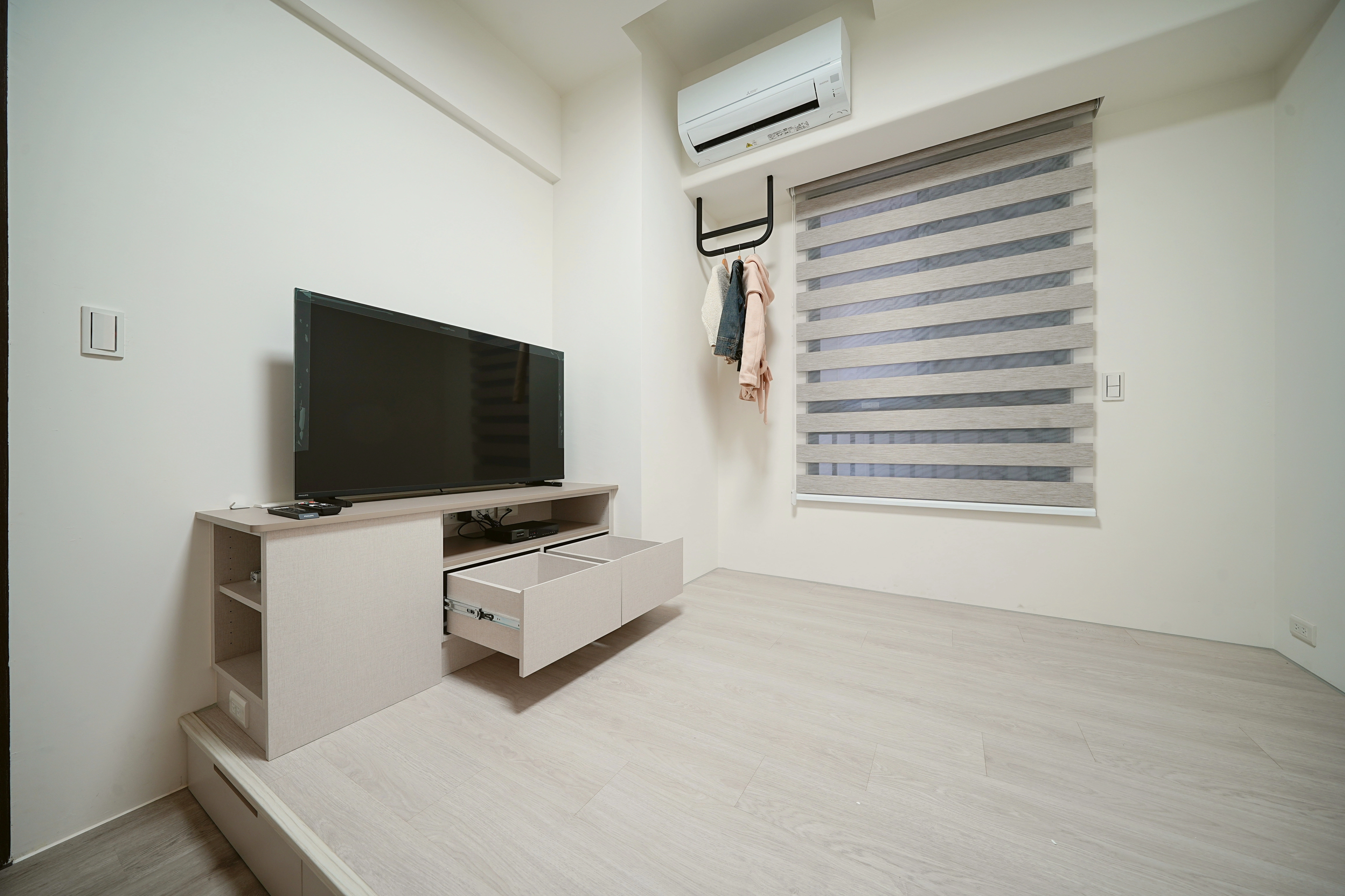 小坪數收納規劃:臥室系統電視櫃配備滑軌抽屜,架高木地板增加大容量收納,打造簡約清爽的機能睡房。