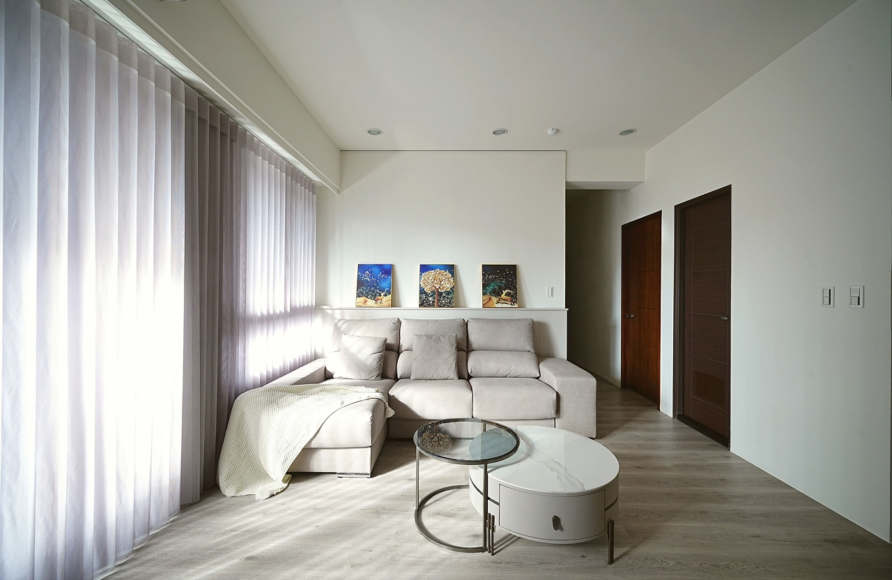 客廳沙發區規劃：簡約白牆裝飾畫與落地窗簾採光，搭配圓形石紋茶几，打造舒適解壓的居家空間。