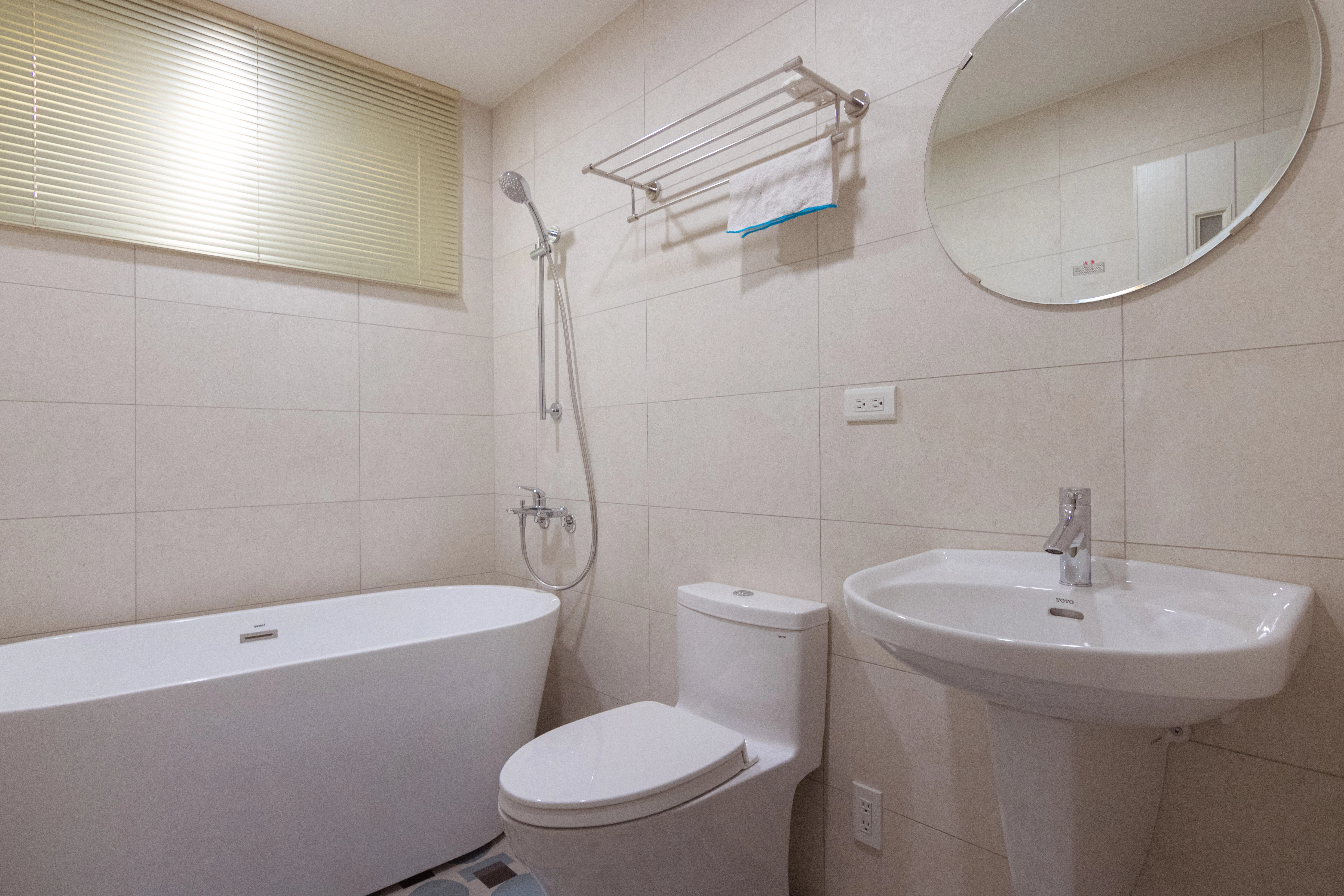 簡約風浴室設計配置獨立式白色浴缸與橢圓浴鏡,搭配質感淺色壁磚,打造飯店式舒適衛浴裝潢美學。