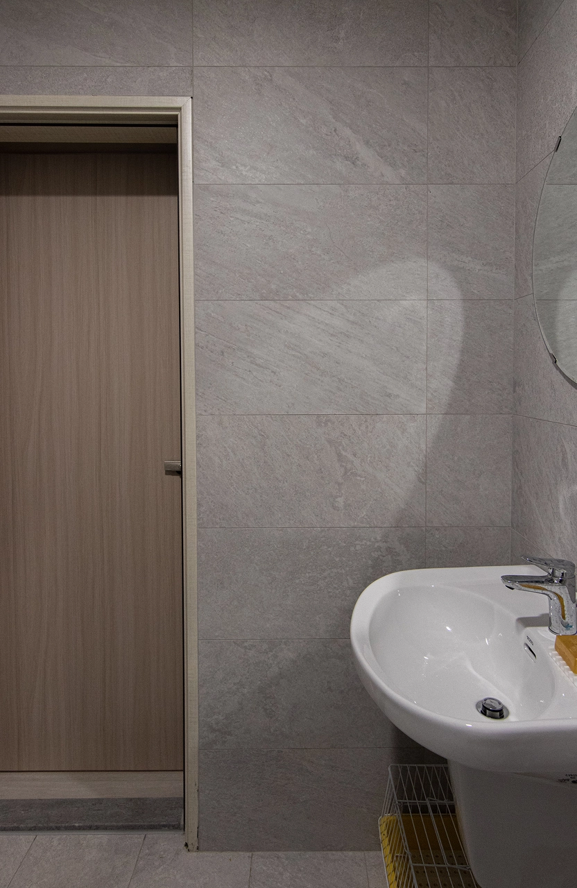 灰色石紋磚浴室，搭配木質門與白色陶瓷洗手盆