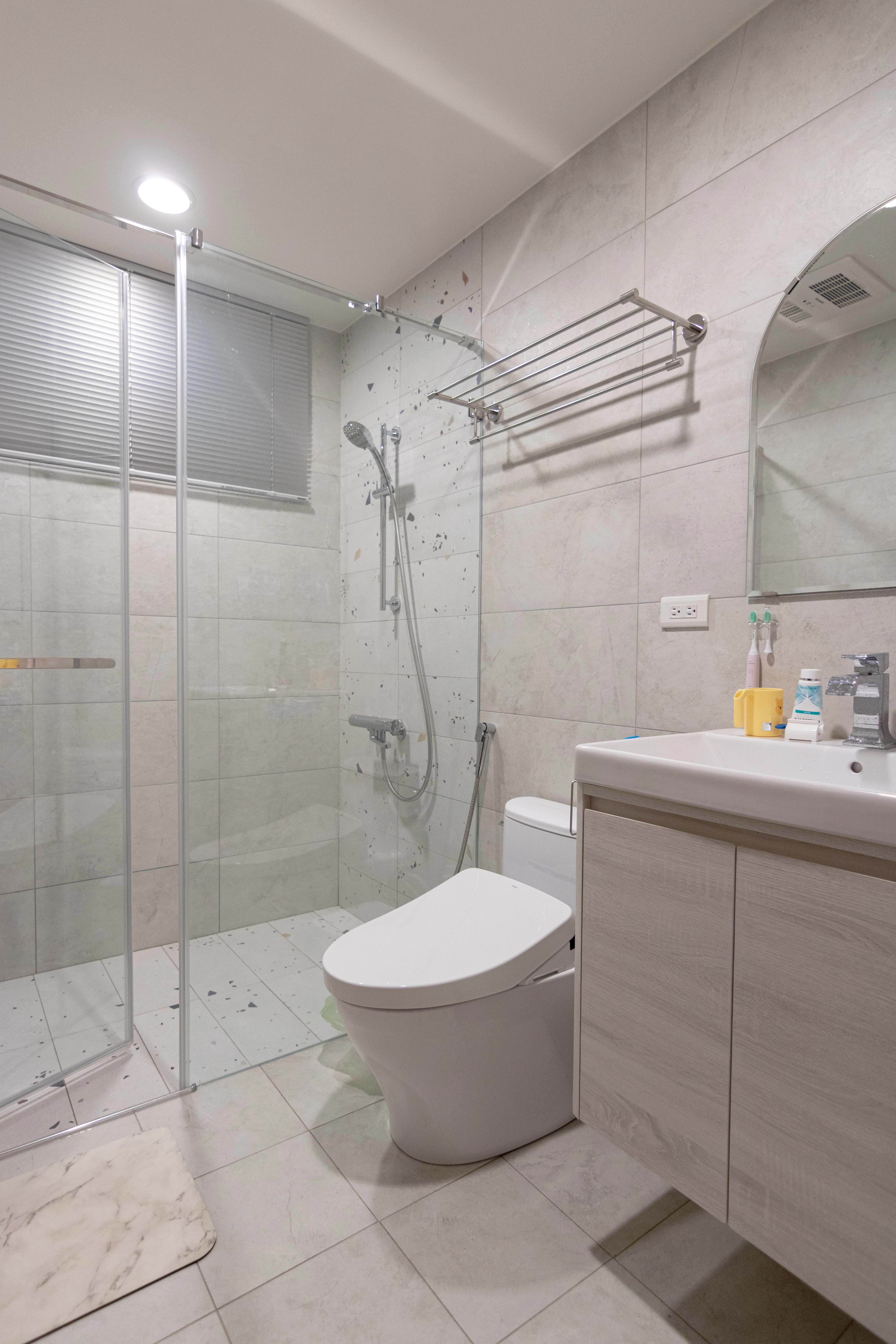 現代風衛浴設計採用玻璃乾濕分離門，搭配質感灰磚與水磨石裝飾，打造簡約乾淨的浴室裝潢空間。