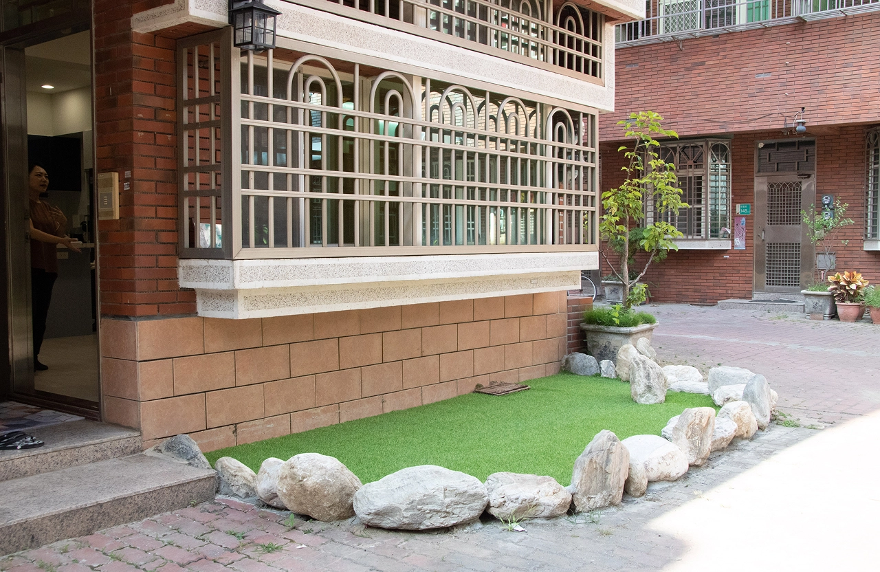 透天住宅戶外花圃美化方案，結合人工草皮、白鵝卵石與景觀植栽規劃，打造低維護且具質感的居家園藝端景。