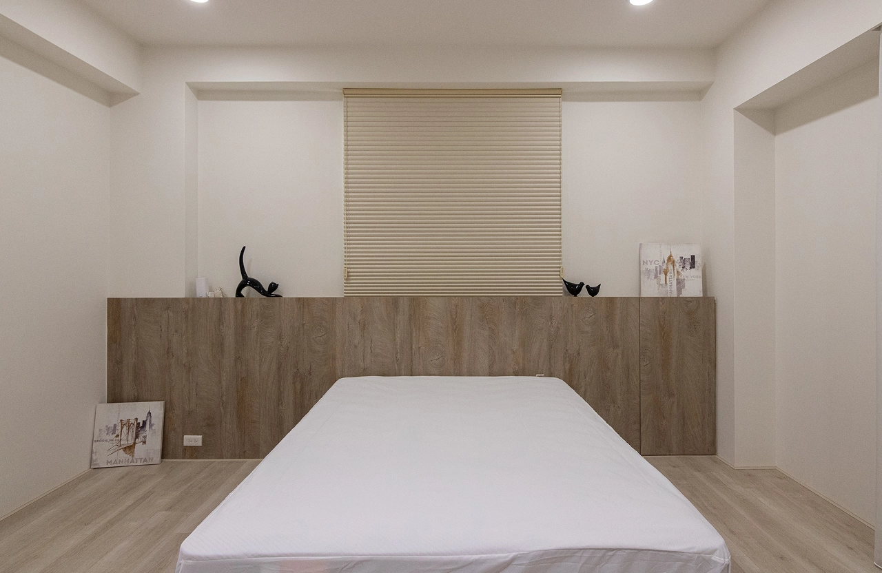 客製化木質床頭背牆具備收納功能，簡約設計化解壓樑問題，完美結合系統家具美學與實用臥室規劃。