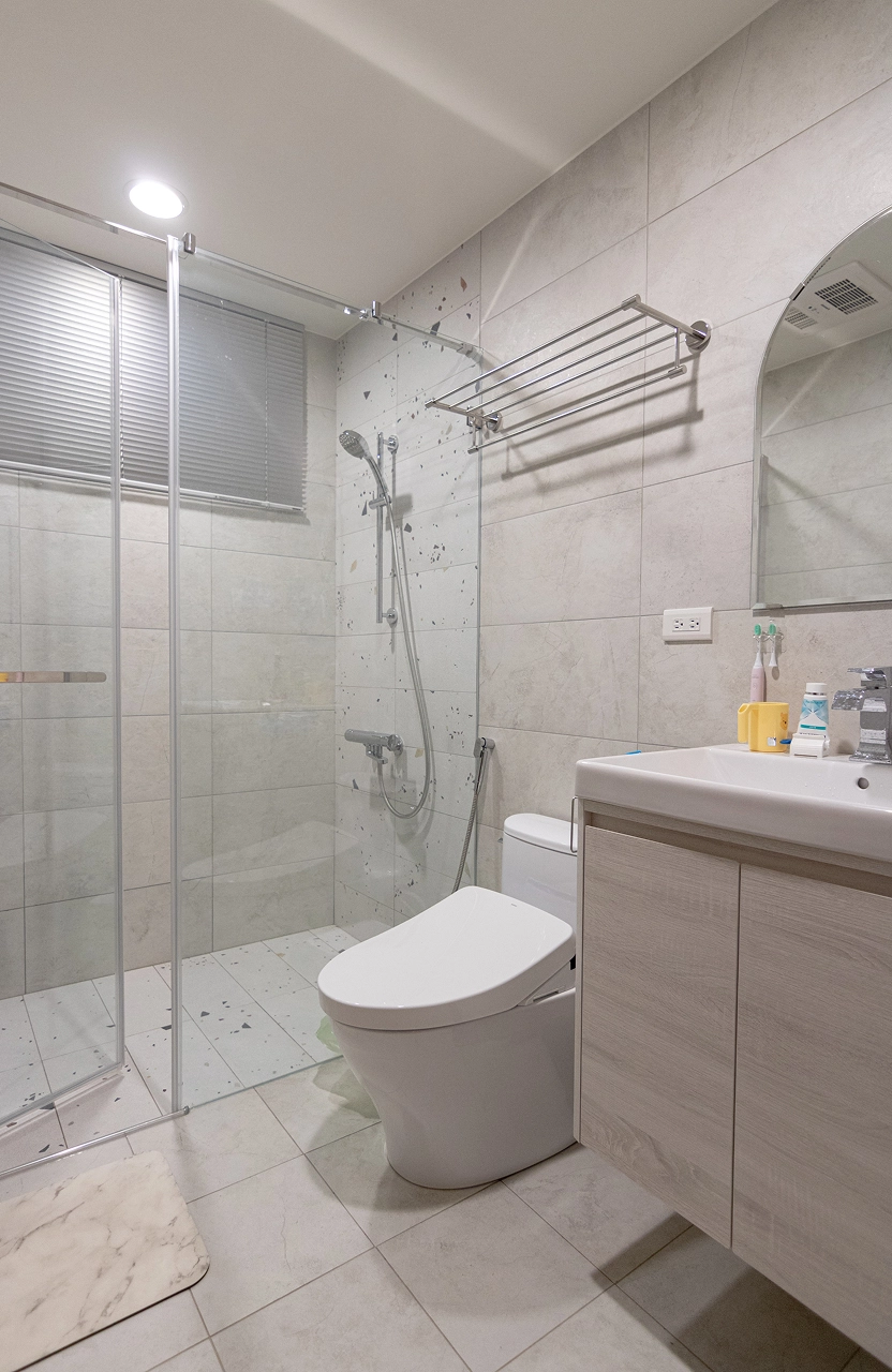 現代風衛浴設計採用玻璃乾濕分離門，搭配質感灰磚與水磨石裝飾，打造簡約乾淨的浴室裝潢空間。