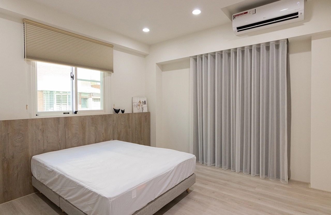 北歐風臥室設計採用淺木色系統床頭背牆，搭配超耐磨木地板與落地窗簾，營造自然舒適的居家裝潢氛圍。