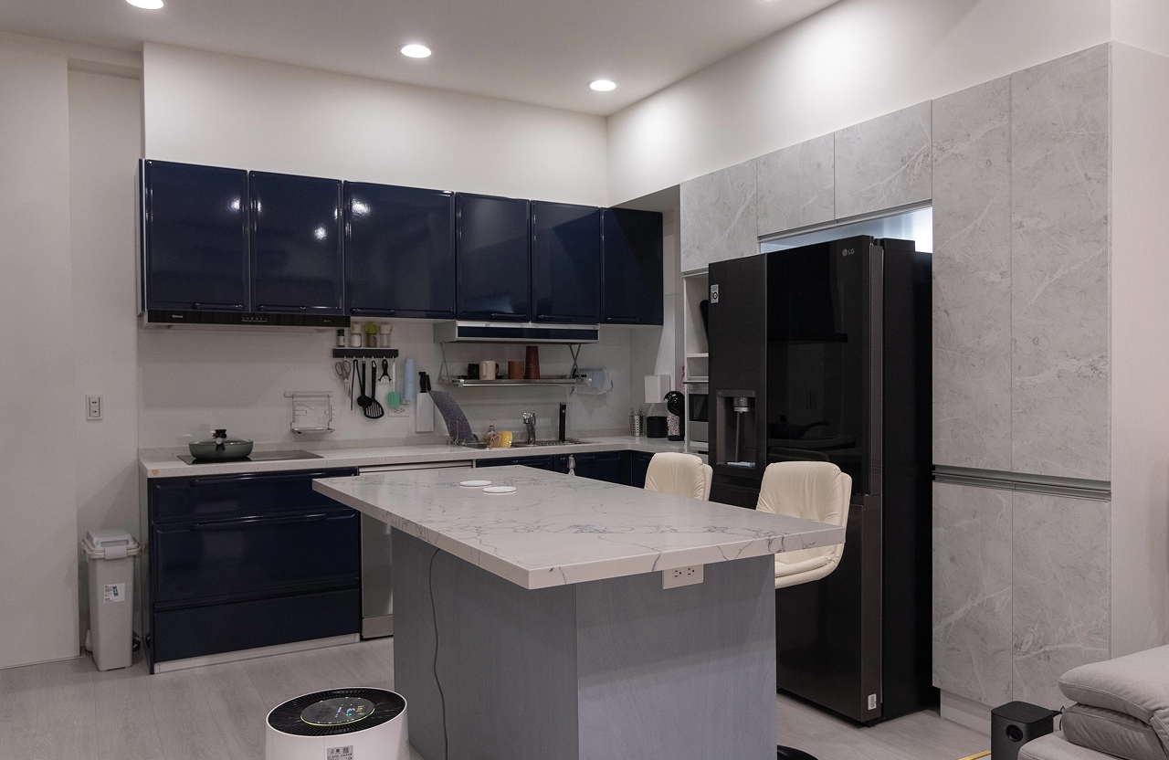 德盈廚房設計：中古屋翻新選用深藍亮面櫥櫃，內嵌式冰箱與中島插座規劃，極大化餐廚空間收納機能。