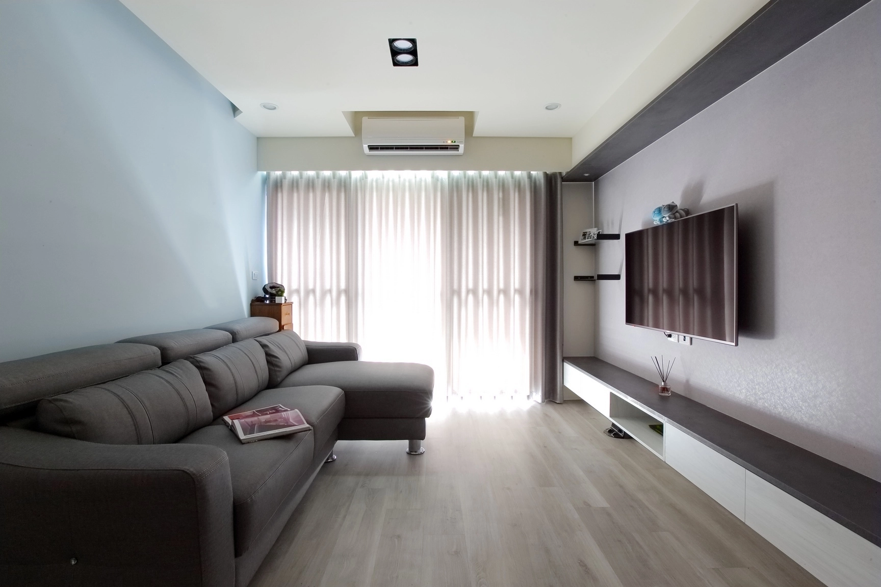 德盈設計客廳案例:灰系L型沙發配現代感電視牆,落地窗光線通透雅緻。