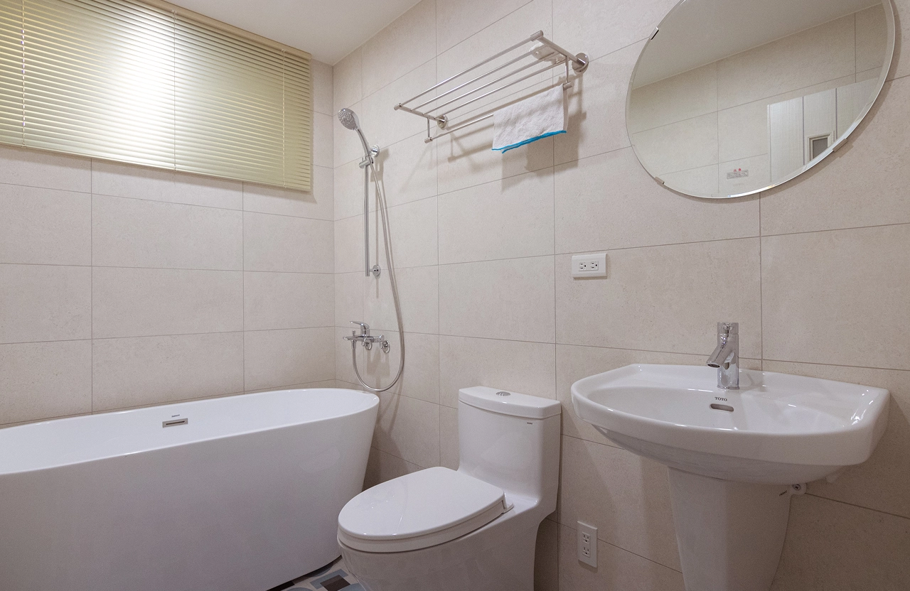 簡約風浴室設計配置獨立式白色浴缸與橢圓浴鏡，搭配質感淺色壁磚，打造飯店式舒適衛浴裝潢美學。