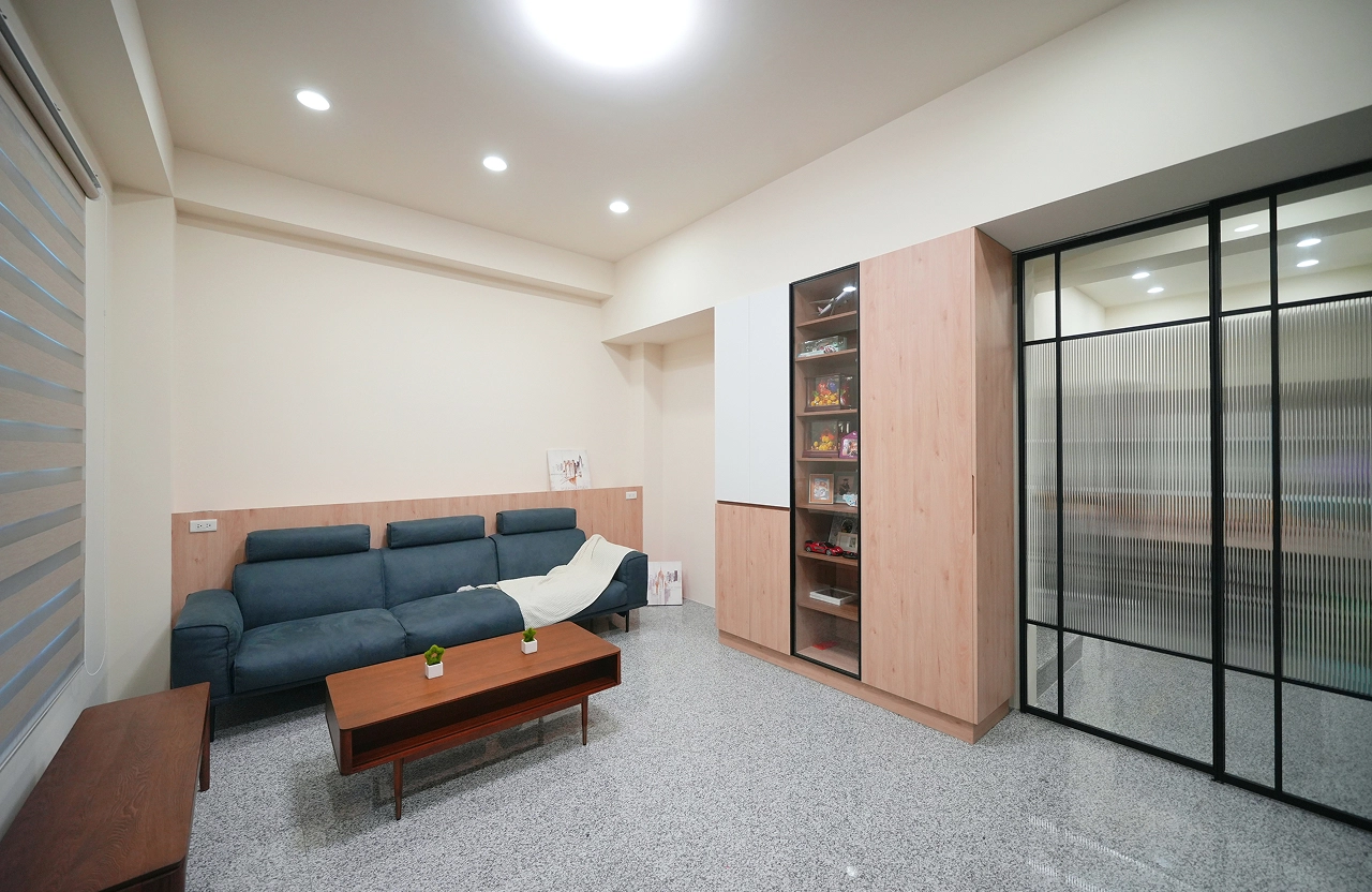 新成屋客廳以木紋系統櫃搭配黑框玻璃推拉門，精準配置裝修預算