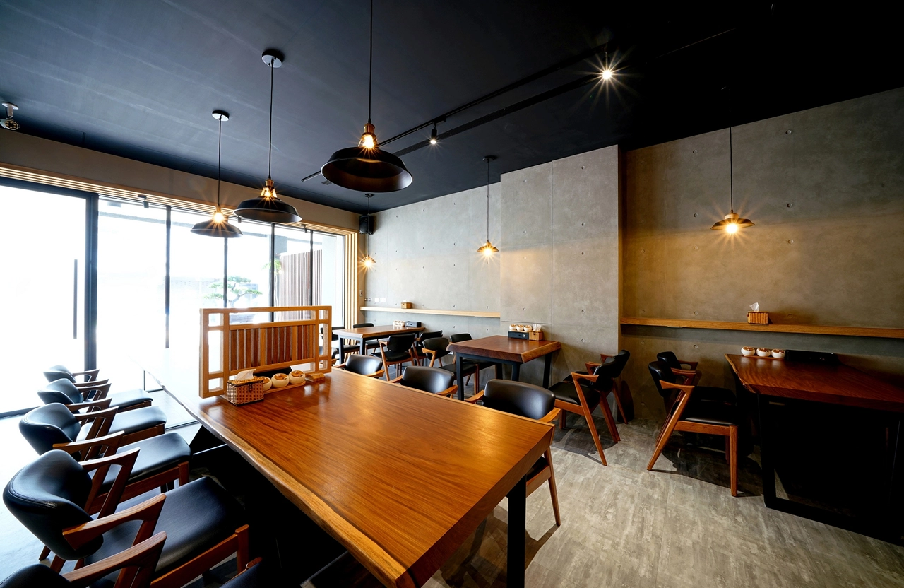 商業空間裝潢案例：餐廳落地窗引進自然採光，黑色工業風燈飾點亮實木餐桌，呈現簡約沉穩的日式設計氛圍。
