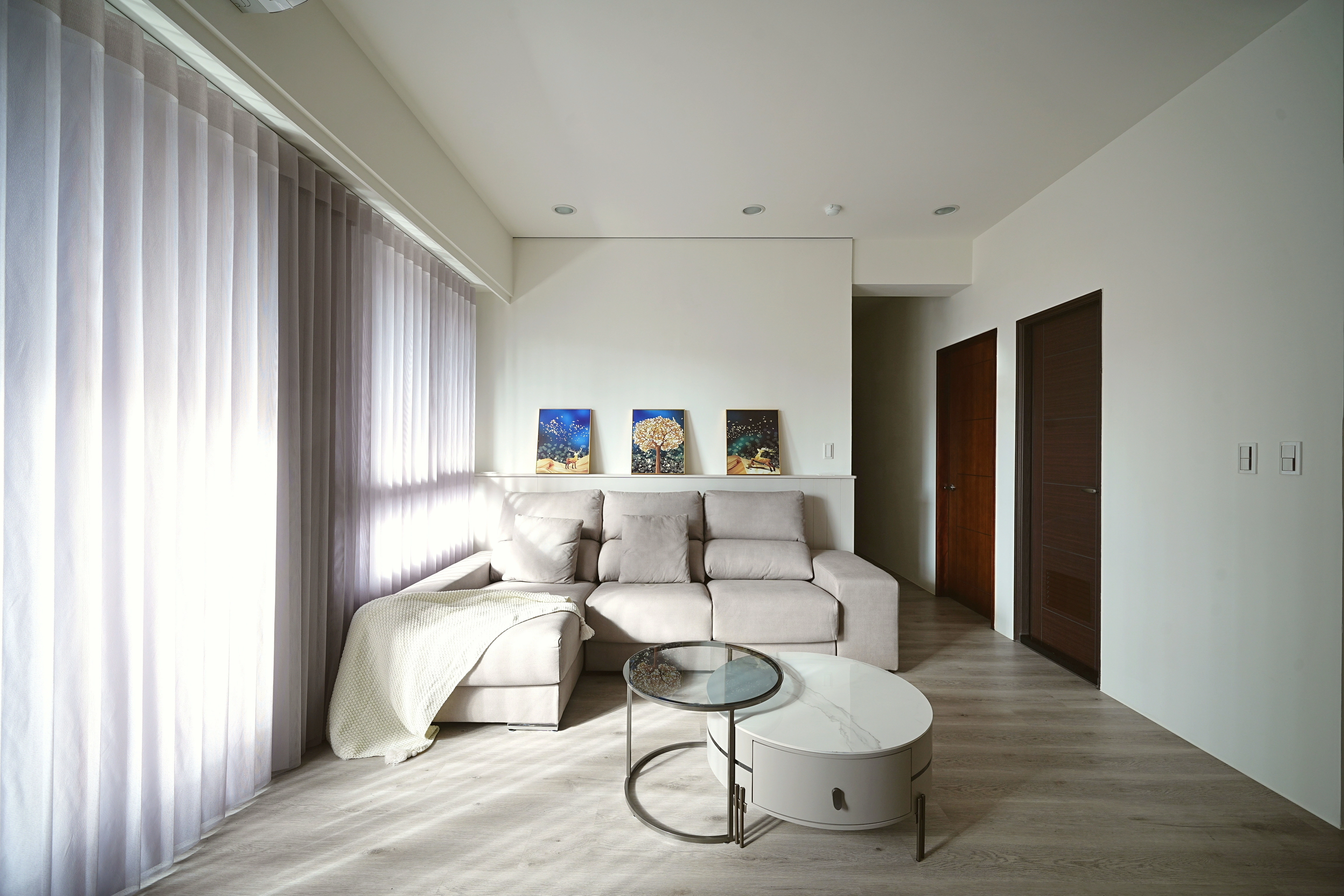 客廳沙發區規劃:簡約白牆裝飾畫與落地窗簾採光,搭配圓形石紋茶几,打造舒適解壓的居家空間。