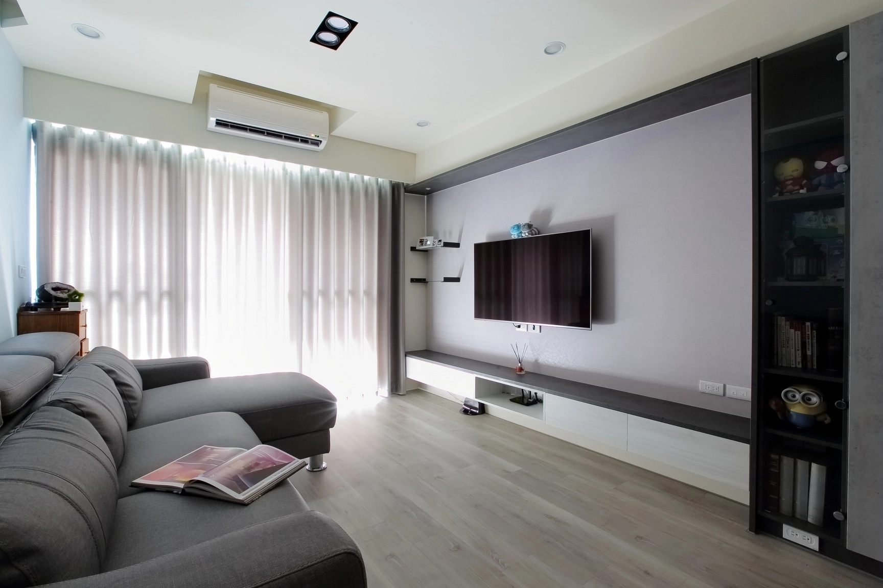 德盈現代簡約客廳:灰色沙發與木地板,系統高櫃收納公仔,空間淨亮大氣。